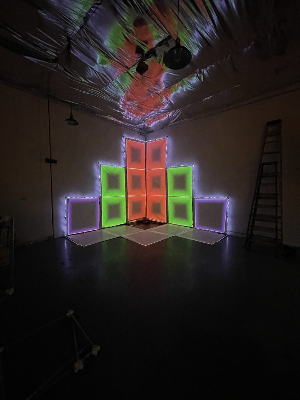 A symmetrical wall of glowing translucent panels under a mirrored ceiling, with no one in the room.