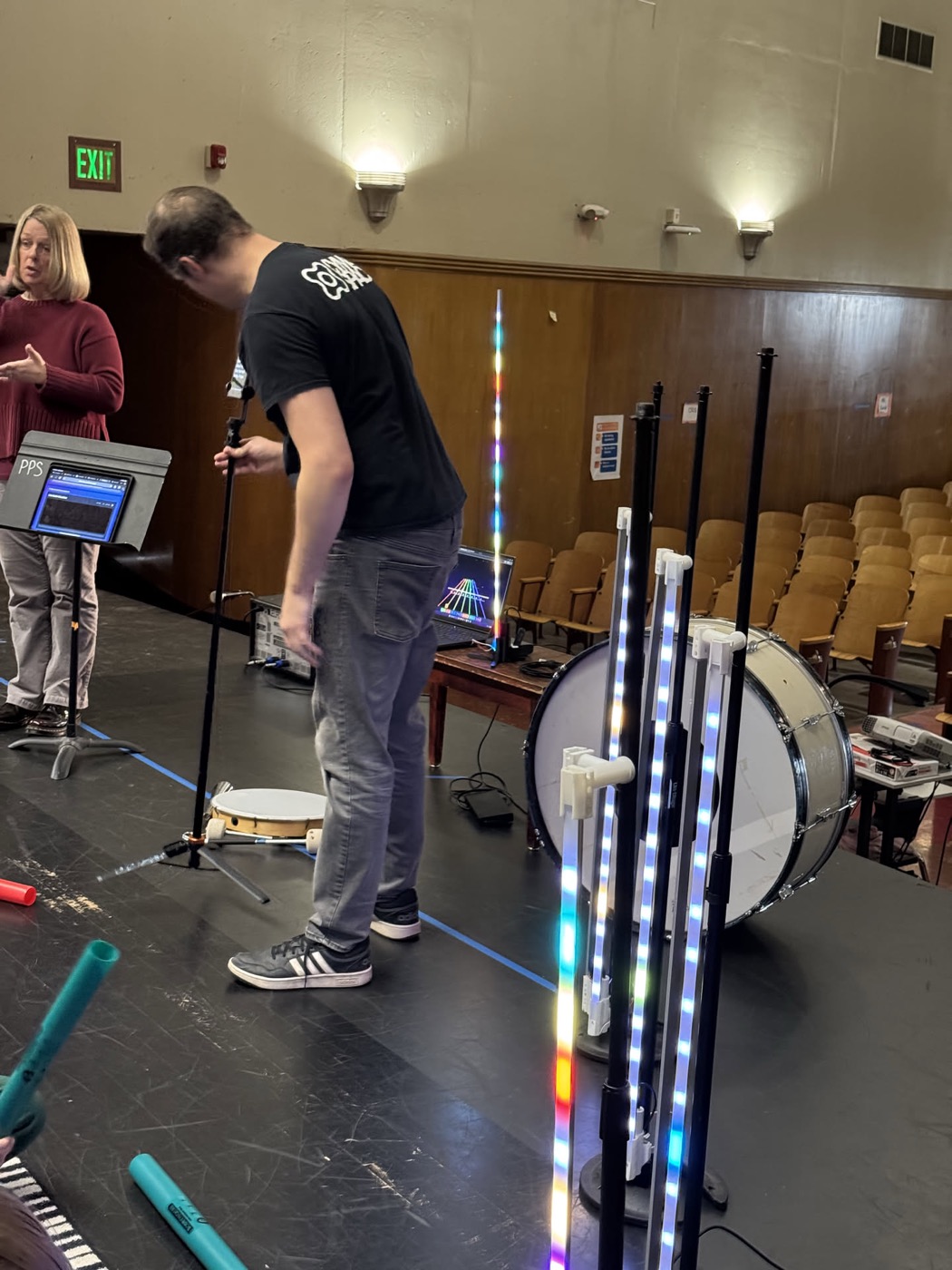 The team standing a light tube upright and moving a bass drum into position on the stage.