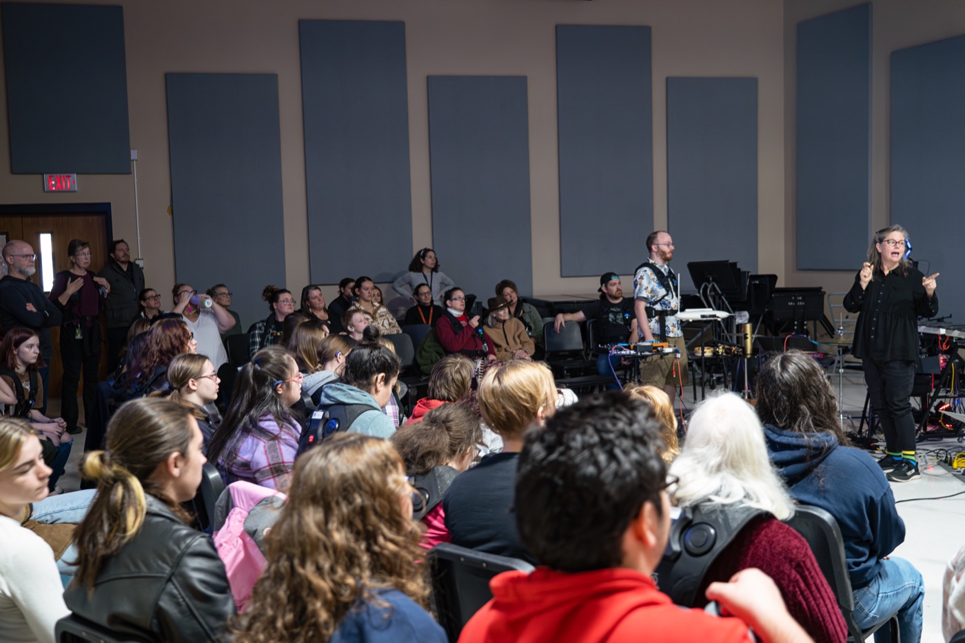 An ASL interpreter signs at the front of a full lecture room at Southern Oregon University while a presenter stands beside demonstration equipment and about forty people watch.