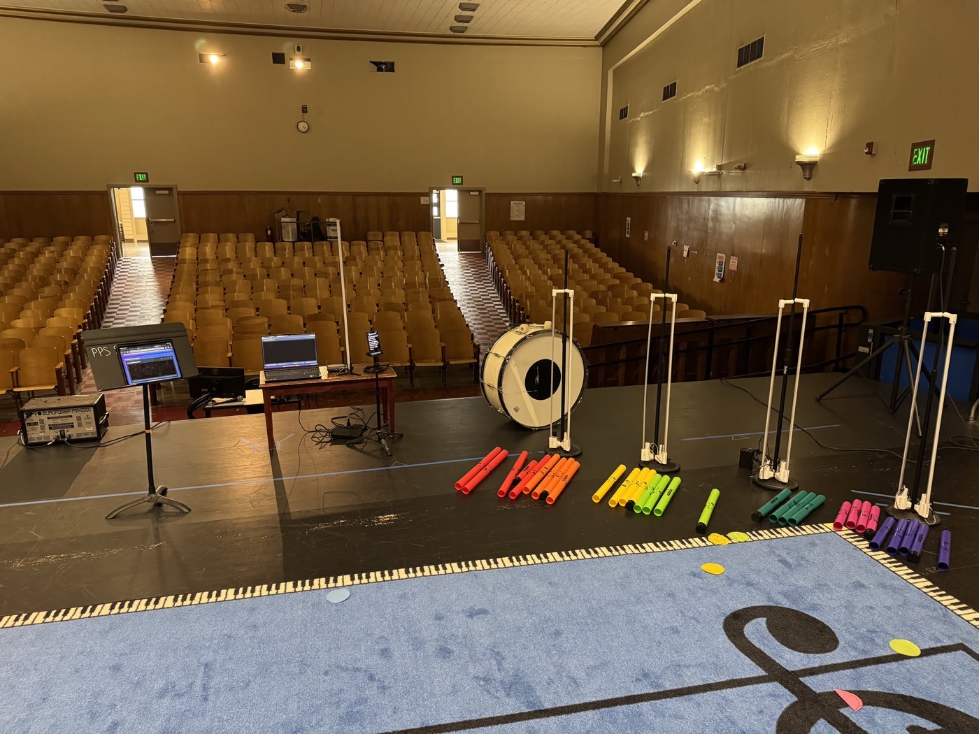 A floor mat printed with a large musical staff holds a gong, two freestanding light tubes, and a row of color coded bars laid out like a keyboard.